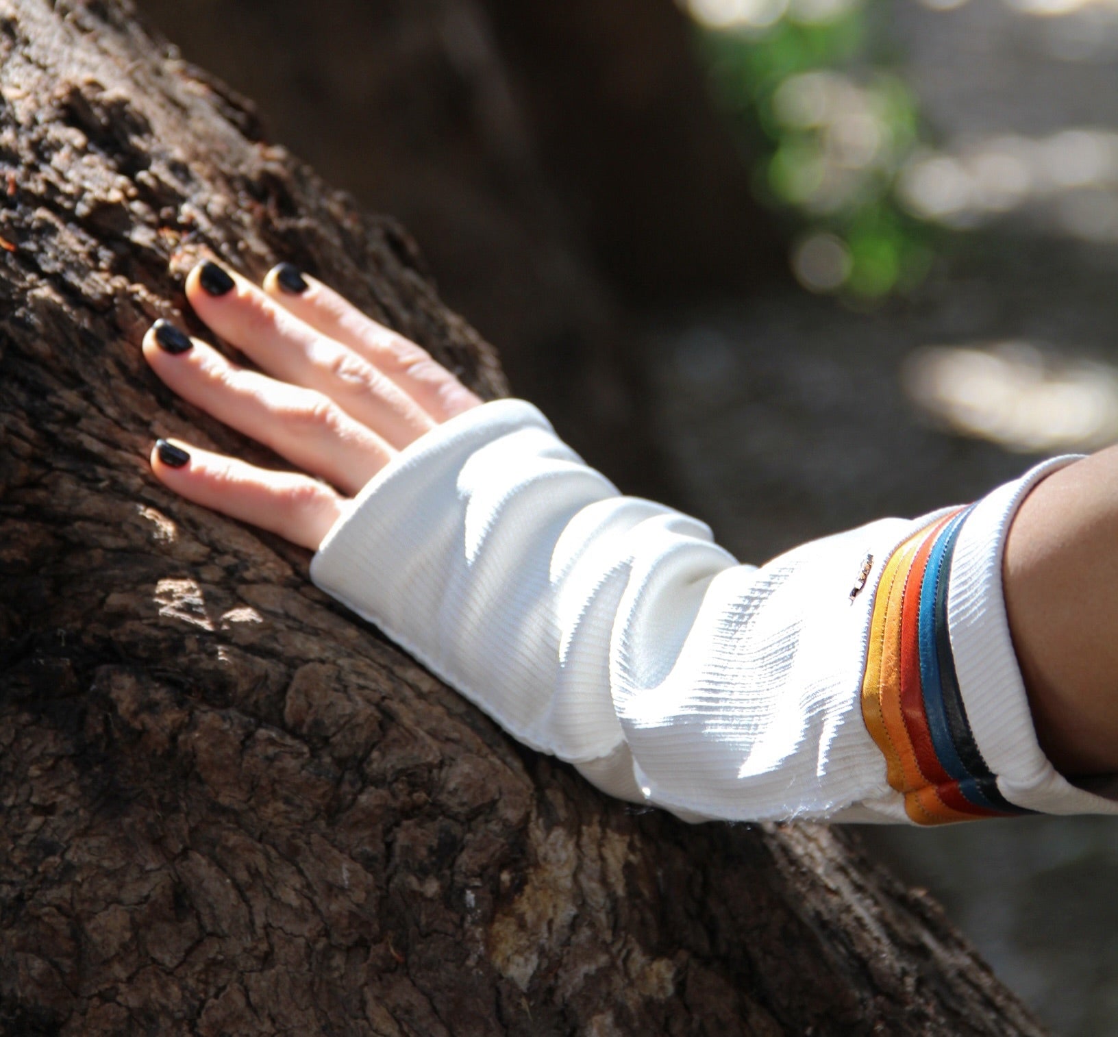 Roxy 81 white long fingerless leather gloves with striped cuff resting on tree bark