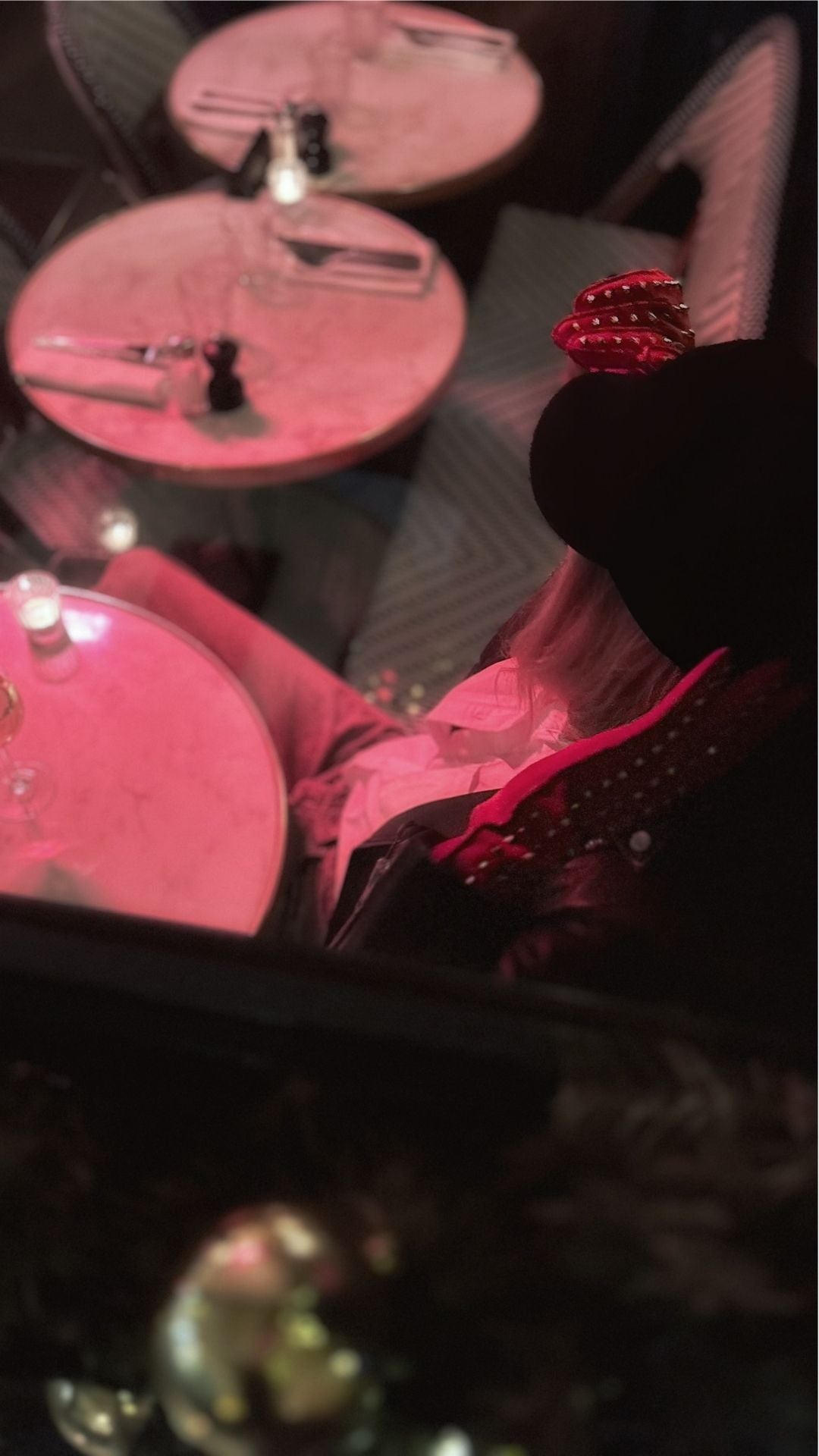 Overhead view of a woman seated at a café table under pink evening light, wearing red leather gloves.