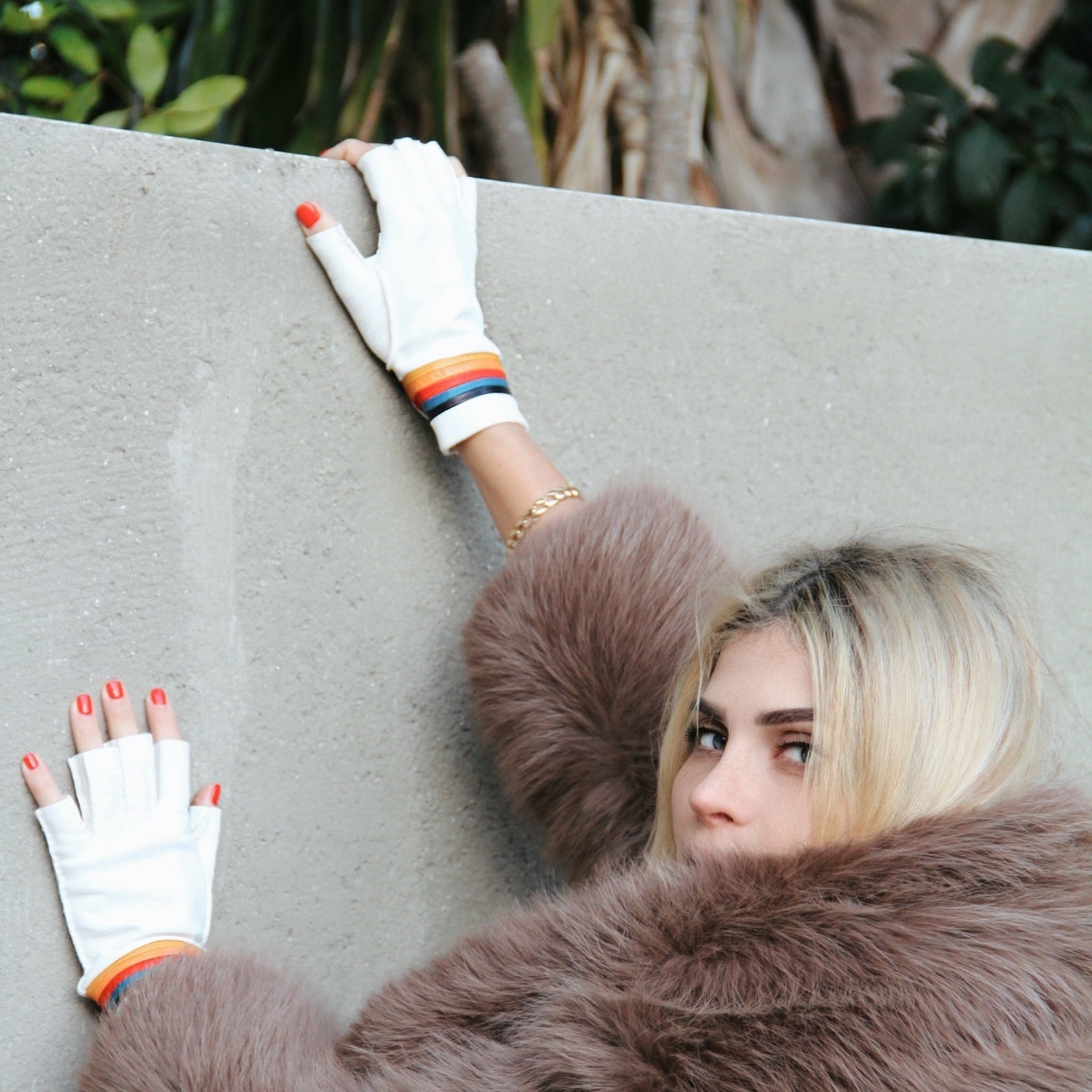 Person wearing a fur coat and gloves against a neutral background