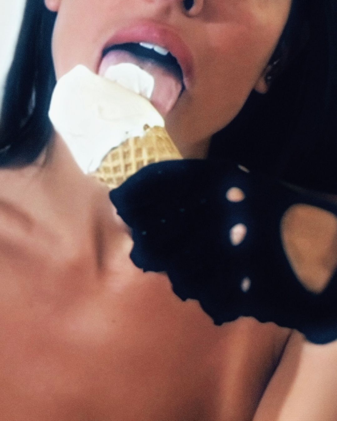 Close-up of a woman licking a vanilla ice cream cone, wearing black suede gloves with cutouts.