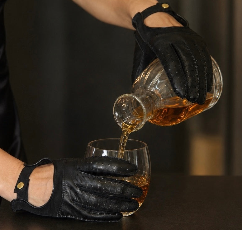 Black leather fingerless gloves with gold snap pouring whisky into a glass