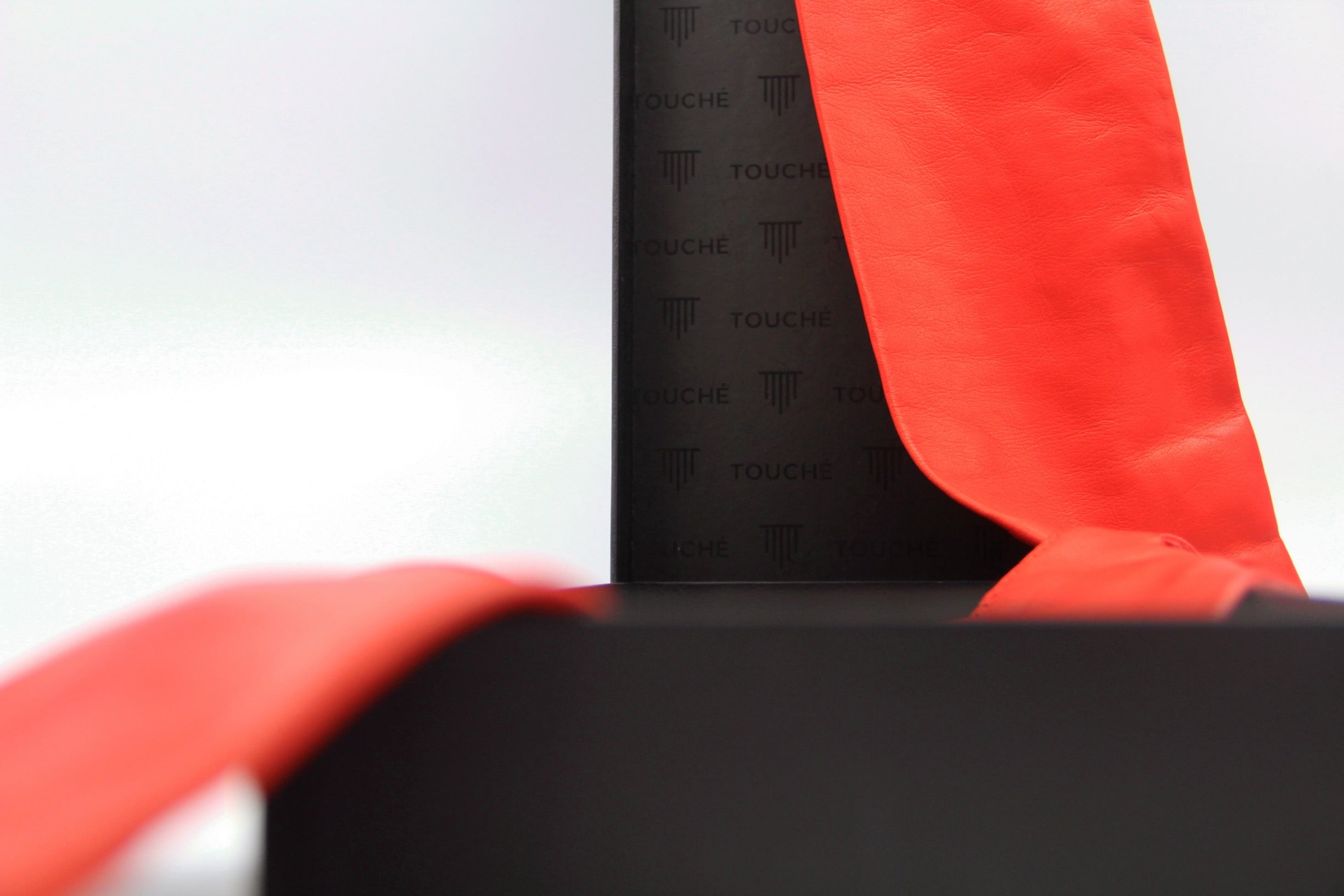 Red leather glove draped over a black Touché gift box with branded lining. Focus on contrast between luxury leather and minimalist packaging.