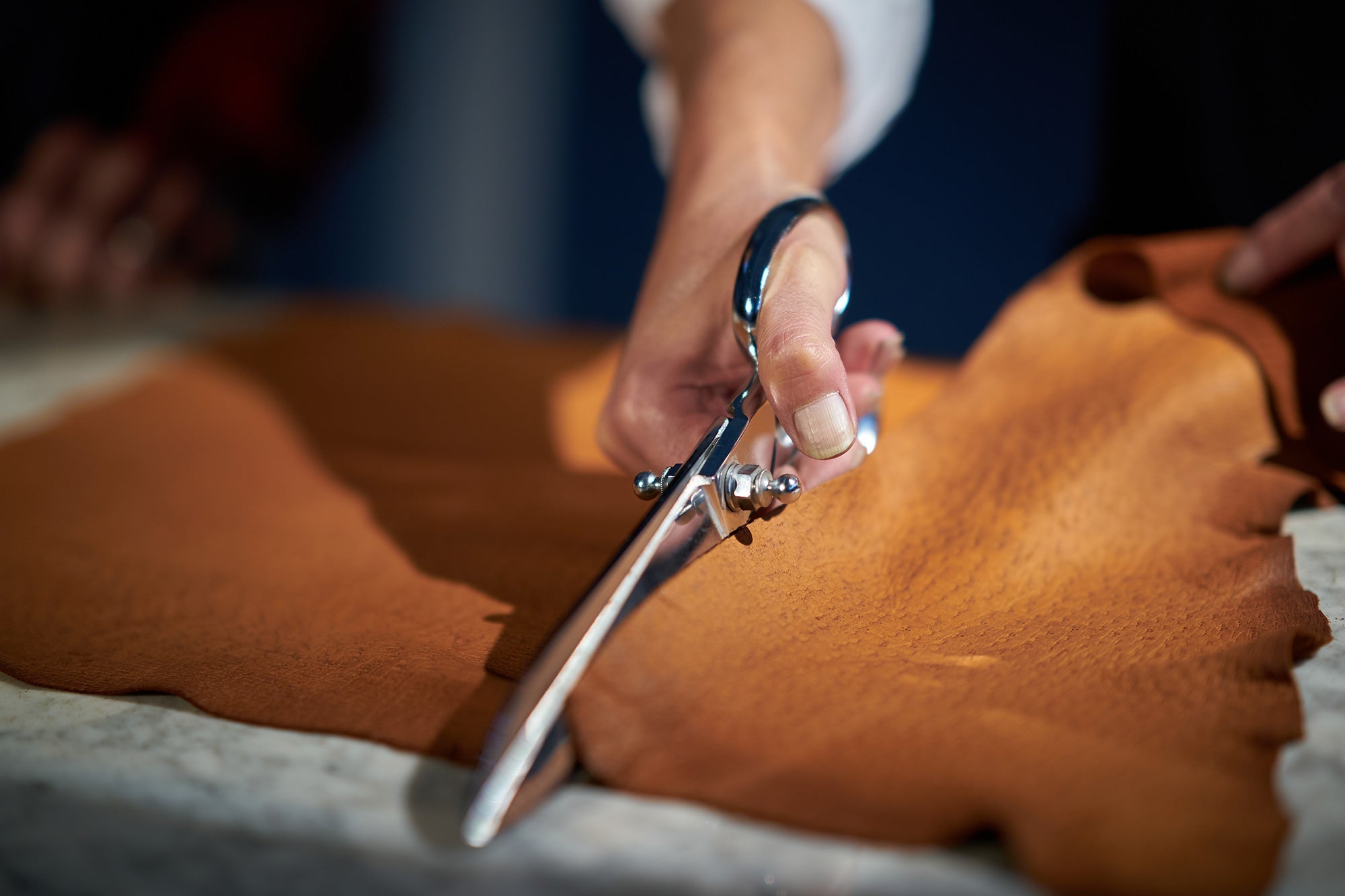 A close-up of a skilled artisan’s hand carefully cutting leather with a precision blade, marking the beginning of the glove-making process.